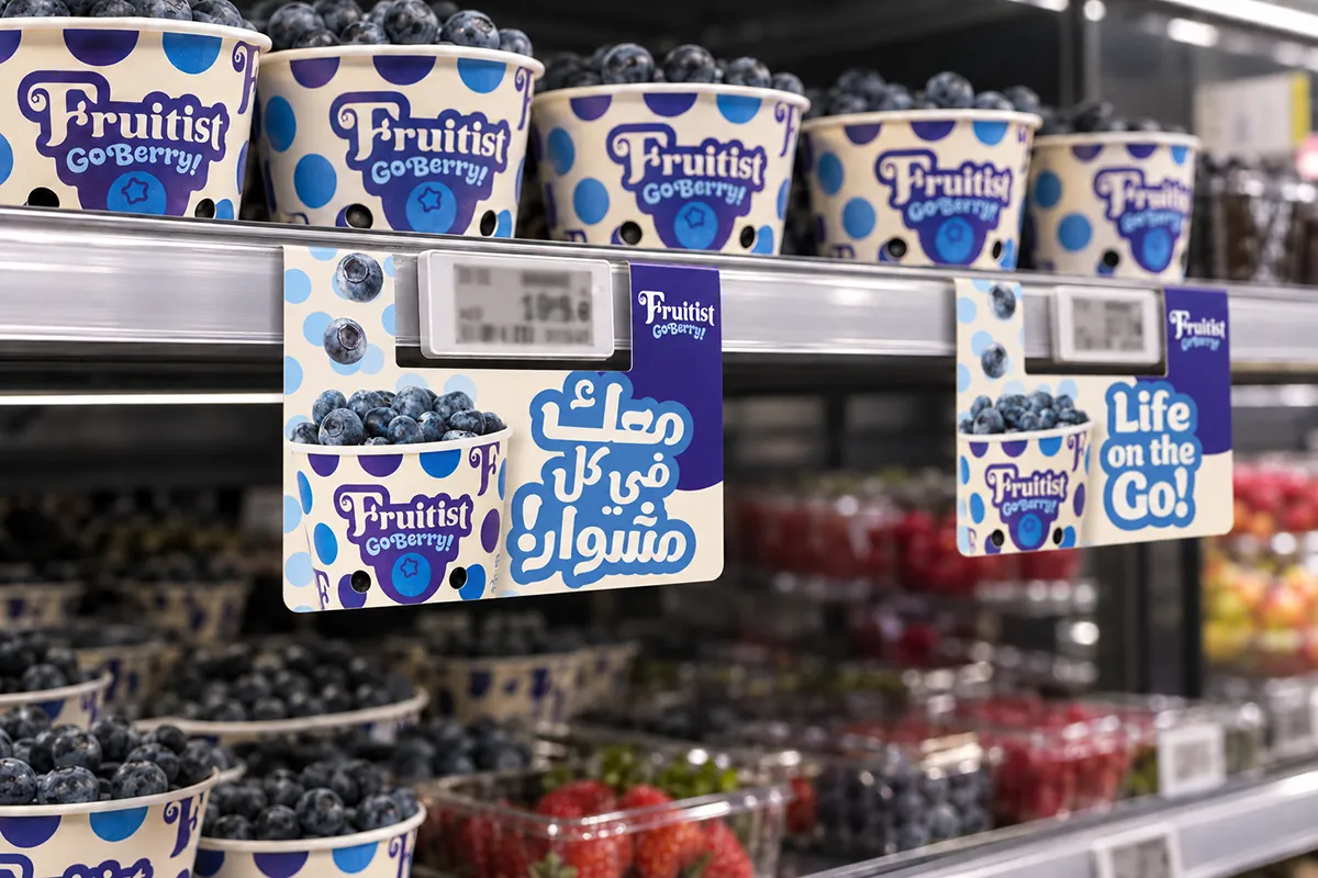 Illustrative refrigerated-shelf mockup of Fruitist GoBerry! shelf talkers featuring «معك في كل مشوار!» and ‘Life on the Go!’ beneath blueberry cups.